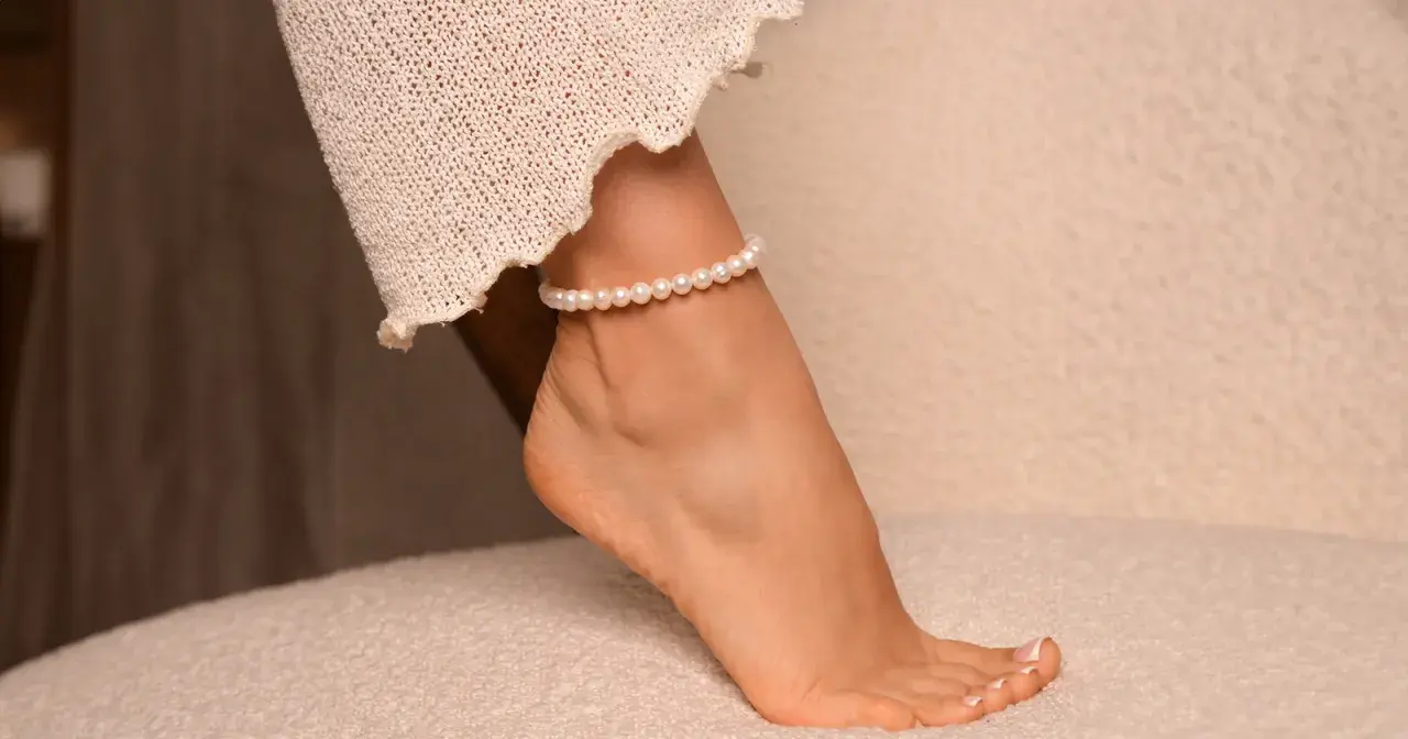 Delikatna bransoletka z pereł na prawej nodze, ozdobiona koronkową tkaniną, dodaje elegancji.