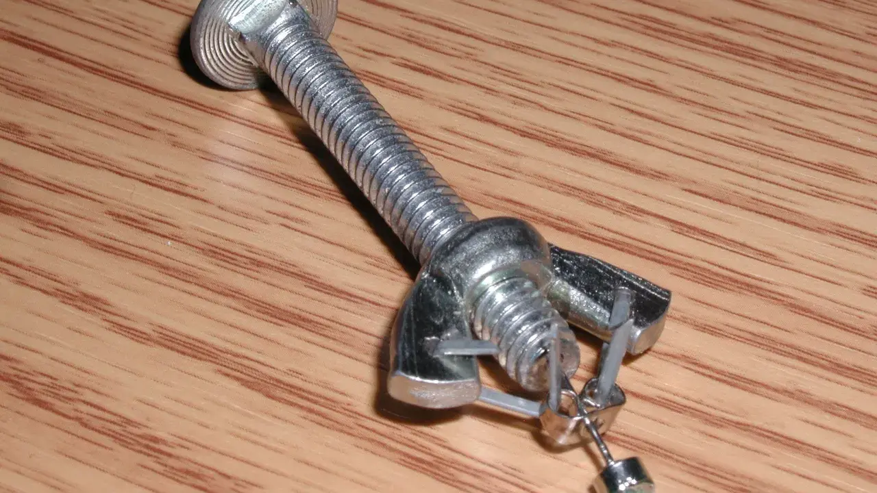 Jak zdjąć kolczyki wkręty? Metalowy element imitujący śrubę z nakrętką i zaczepem, na którym wisi mały kolczyk.