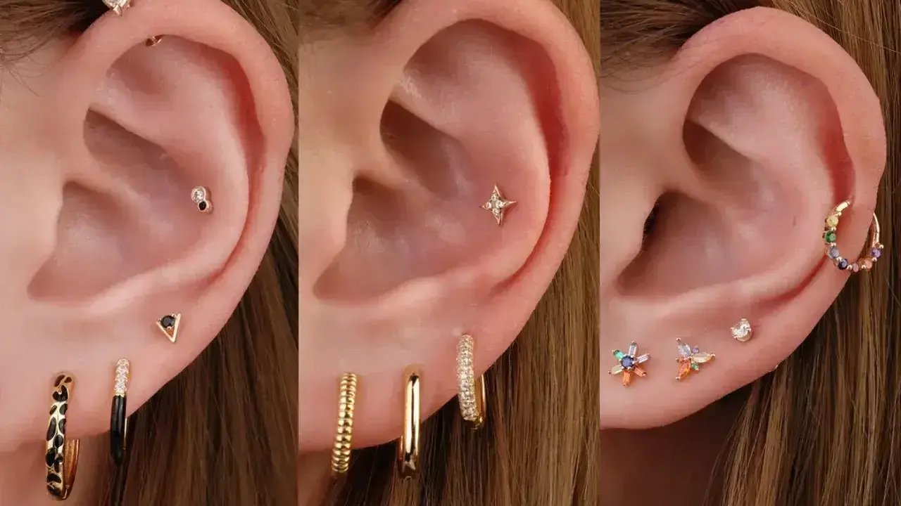 Ucho z wieloma kolczykami: helix, płatek, tragus. Złote, kolorowe, z cyrkoniami.