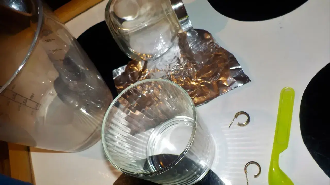 Przygotowania do czyszczenia złota folią aluminiową: szklanka, słoik, folia, łyżeczka i kolczyki.