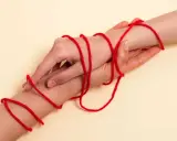 Dwie dłonie splecione czerwoną nitką, symbolizującą więź. Co oznacza czerwona nitka na nadgarstku? To znak ochrony i połączenia.
