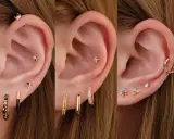 Ucho z wieloma kolczykami: helix, płatek, tragus. Złote, kolorowe, z cyrkoniami.