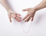Dwie dłonie, połączone zerwaną czerwoną nitką, symbolizują nieprzerwane więzi.