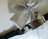 Elegancka bransoleta z czarnym paskiem i metalowymi elementami, ozdobiona srebrną kokardą. Idealnie pokazuje, jak zapakować biżuterię na prezent.