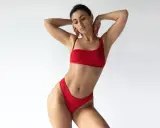 Kobieta w czerwonym bikini o figurze gruszki, z rękami za głową, prezentuje się jak gwiazda.