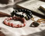 Dwie bransoletki, różowa i czarna, leżą obok złotego pierścionka. Co oznacza czarna bransoletka? Może symbolizować siłę i elegancję.
