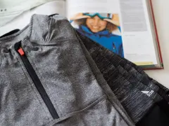 Szara bluza sportowa z zamkiem i czarnymi wstawkami, obok otwartej książki. Materiał to poliamid a poliester, idealny na zimowe sporty.