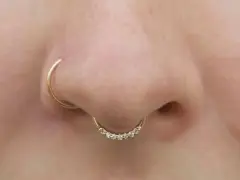 Złoty kolczyk w nosie, ozdobiony cyrkoniami, dodaje uroku. To subtelne rhino piercing.