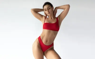 Kobieta w czerwonym bikini o figurze gruszki, z rękami za głową, prezentuje się jak gwiazda.