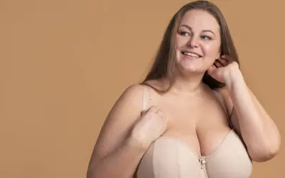 Uśmiechnięta kobieta w beżowym biustonoszu, który podkreśla jej idealny rozmiar biustu.