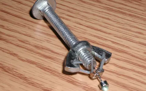 Jak zdjąć kolczyki wkręty? Metalowy element imitujący śrubę z nakrętką i zaczepem, na którym wisi mały kolczyk.