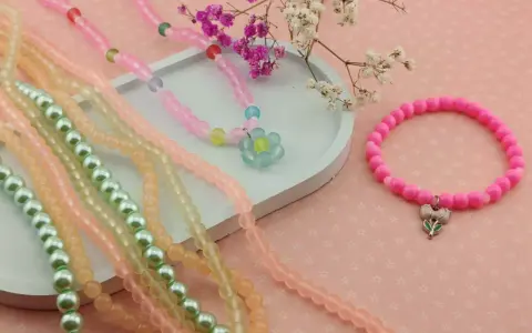 Kolorowe koraliki do bransoletek: naszyjnik z kwiatkiem, różowa bransoletka z zawieszką, zielone i pomarańczowe sznurki.