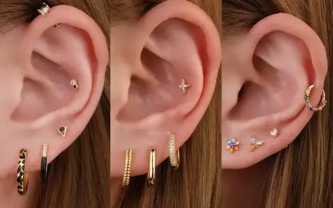 Ucho z wieloma kolczykami: helix, płatek, tragus. Złote, kolorowe, z cyrkoniami.