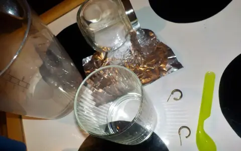 Przygotowania do czyszczenia złota folią aluminiową: szklanka, słoik, folia, łyżeczka i kolczyki.