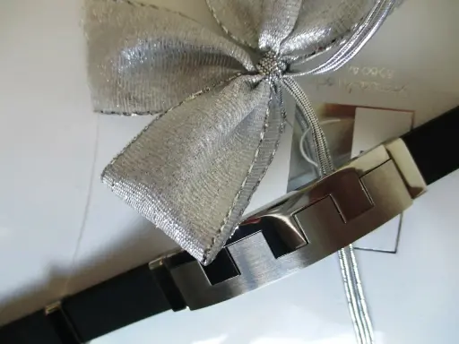 Elegancka bransoleta z czarnym paskiem i metalowymi elementami, ozdobiona srebrną kokardą. Idealnie pokazuje, jak zapakować biżuterię na prezent.