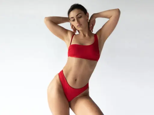 Kobieta w czerwonym bikini o figurze gruszki, z rękami za głową, prezentuje się jak gwiazda.