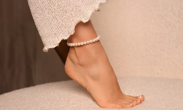 Delikatna bransoletka z pereł na prawej nodze, ozdobiona koronkową tkaniną, dodaje elegancji.
