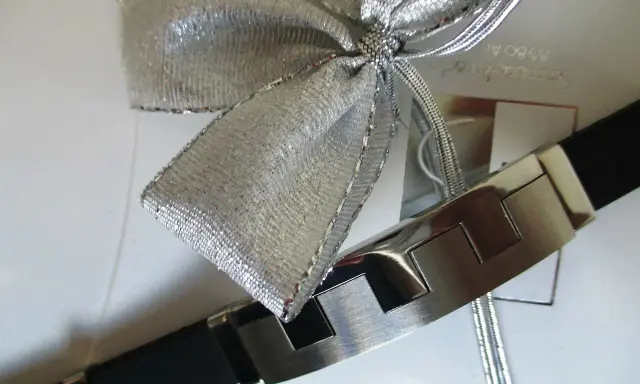 Elegancka bransoleta z czarnym paskiem i metalowymi elementami, ozdobiona srebrną kokardą. Idealnie pokazuje, jak zapakować biżuterię na prezent.