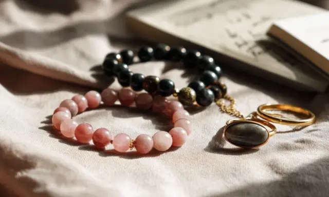 Dwie bransoletki, różowa i czarna, leżą obok złotego pierścionka. Co oznacza czarna bransoletka? Może symbolizować siłę i elegancję.